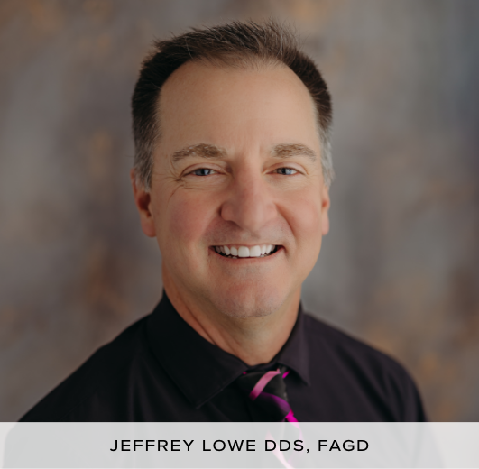 Doctor Jeffrey Lowe DDS, FAGD, smiling in a black shirt with a striped tie against a blurred gray background.
